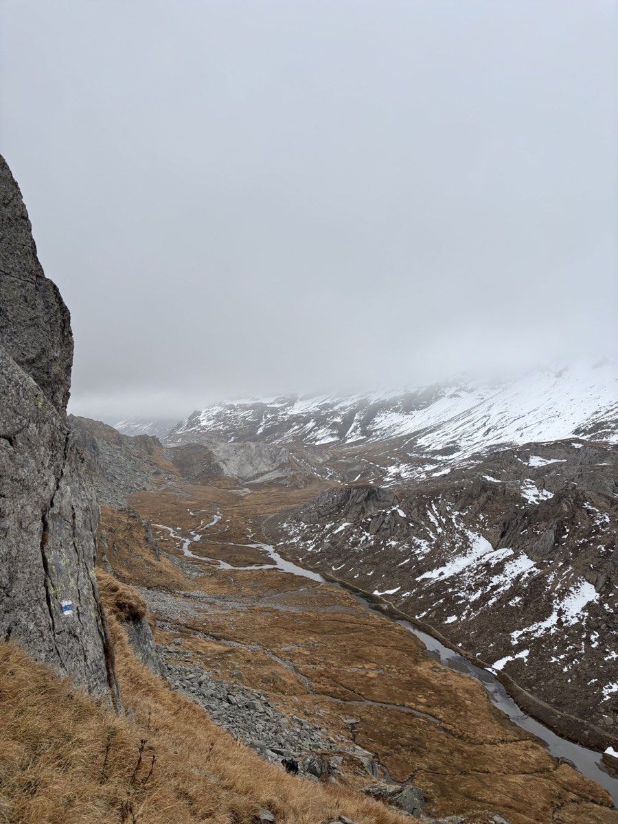 A blue-and-white trail marking above the streams and snow-patched terrain of the Greina