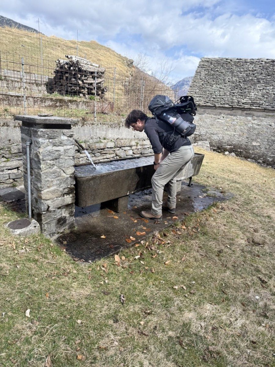 A hiker collecting water from a fountain beside an Alpine settlement
