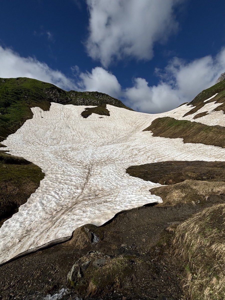 A mountain trail disappearing beneath a broad old snowfield